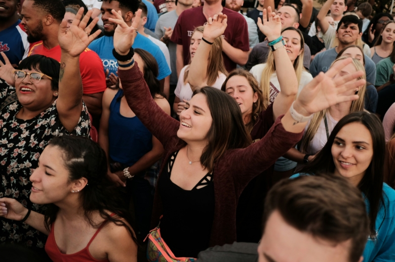 A crowd of young people stand with their arms raised in worship.