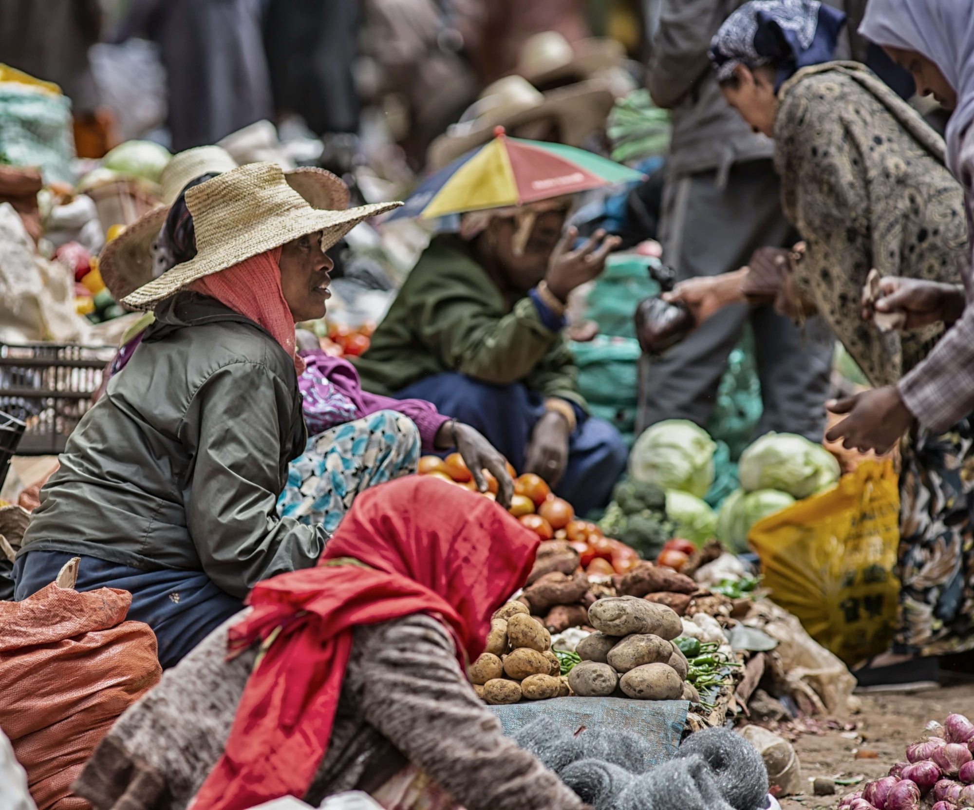 Bustling market stall in Northeast Africa with sellers sitting on the ground with fruit and vegetables on mats in front of them.